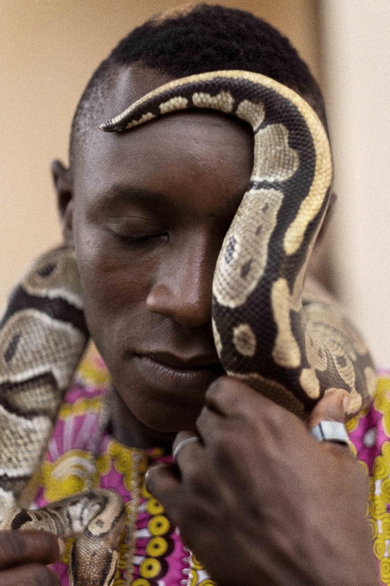 Il guardiano del Tempio dei Pitoni, il più antico luogo sacro del Voodoo, prende in braccio uno dei serpenti custoditi nel Tempio. Ouidah, Repubblica del Benin, 2018.